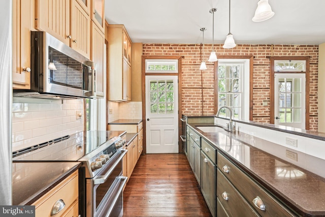 kitchen with a sink, stainless steel appliances, dark stone counters, dark wood-style flooring, and decorative backsplash