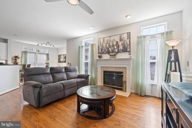living area with light wood finished floors, a fireplace, plenty of natural light, and ceiling fan