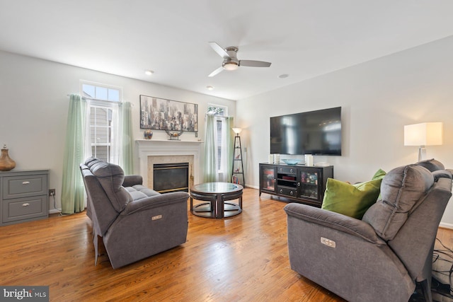 living room with ceiling fan, a glass covered fireplace, and wood finished floors