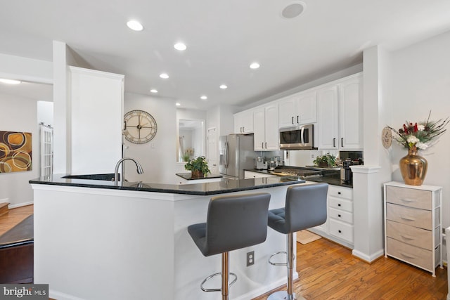 kitchen with stainless steel appliances, a kitchen breakfast bar, light wood finished floors, white cabinets, and recessed lighting