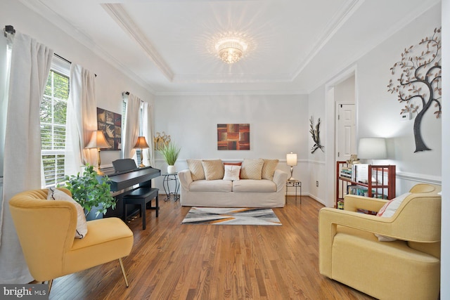 living area with a raised ceiling, wood finished floors, a chandelier, and ornamental molding