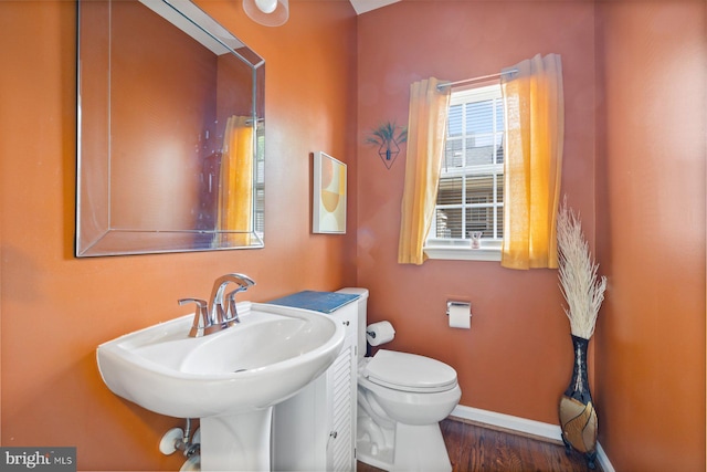 half bathroom featuring baseboards, toilet, wood finished floors, and a sink