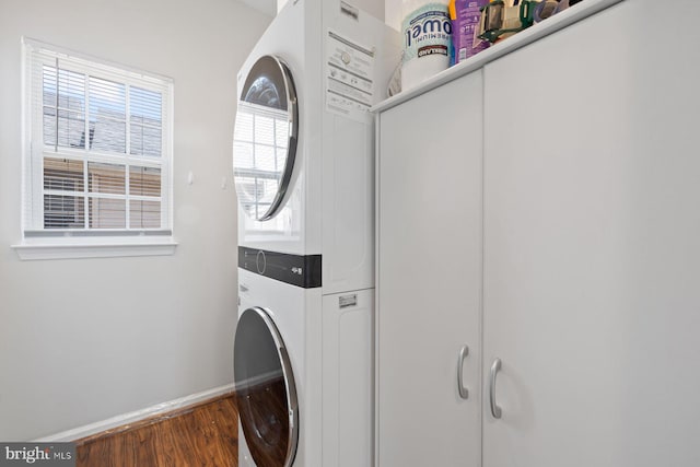 laundry room featuring estacked washer and dryer, baseboards, wood finished floors, and cabinet space
