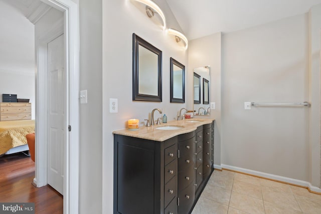 ensuite bathroom featuring baseboards, double vanity, tile patterned floors, and vaulted ceiling