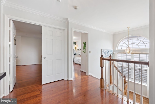 corridor featuring an upstairs landing, wood finished floors, ornamental molding, and baseboards