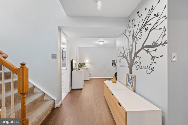corridor featuring wood finished floors, baseboards, and stairs