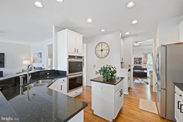 kitchen featuring a sink, stainless steel appliances, white cabinets, light wood finished floors, and dark stone counters