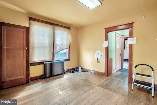 empty room with radiator heating unit, baseboards, and light wood finished floors