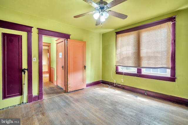 empty room with wood-type flooring, visible vents, a ceiling fan, and baseboards