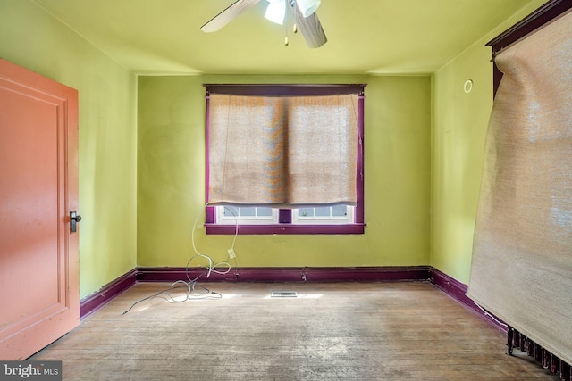empty room featuring wood finished floors, visible vents, baseboards, and ceiling fan