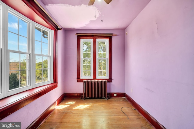 spare room featuring a ceiling fan, baseboards, radiator heating unit, and light wood-type flooring