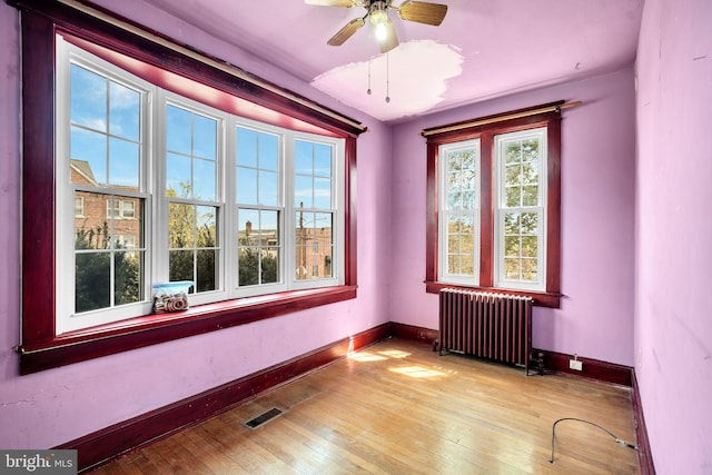 unfurnished room with radiator heating unit, visible vents, wood-type flooring, baseboards, and ceiling fan