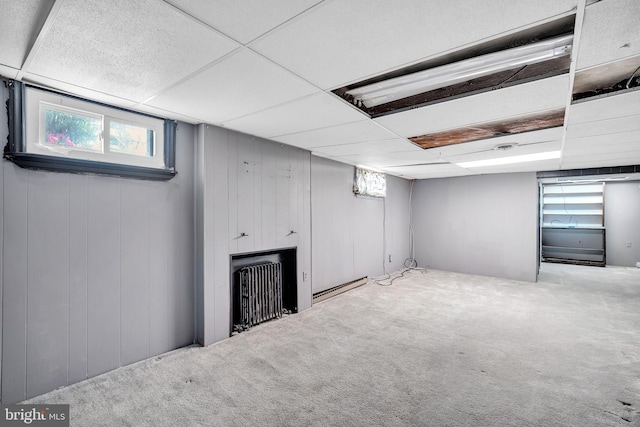 below grade area with a baseboard heating unit, carpet floors, and a paneled ceiling