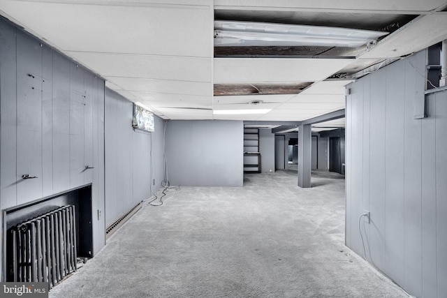 finished basement with radiator heating unit, wooden walls, and carpet flooring