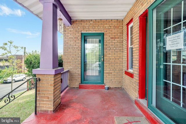 view of exterior entry with a porch and brick siding