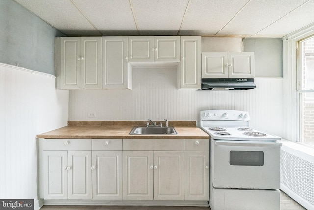 3905 L St, Philadelphia, PA 19124 - kitchen featuring a drop ceiling, under cabinet range hood, a sink, wainscoting, and white electric stove