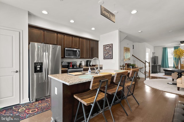 7204 Wood Trail Dr, Lanham, MD 20706 - kitchen featuring an island with sink, a kitchen breakfast bar, dark brown cabinets, appliances with stainless steel finishes, and light stone counters