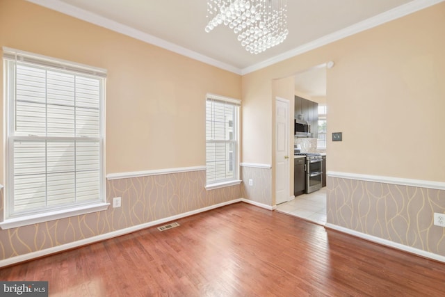 spare room with crown molding, wainscoting, an inviting chandelier, light wood finished floors, and visible vents
