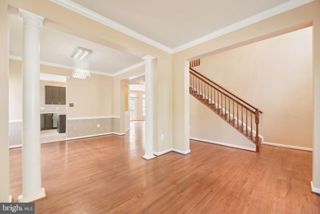unfurnished living room with stairway, crown molding, wood finished floors, an inviting chandelier, and ornate columns
