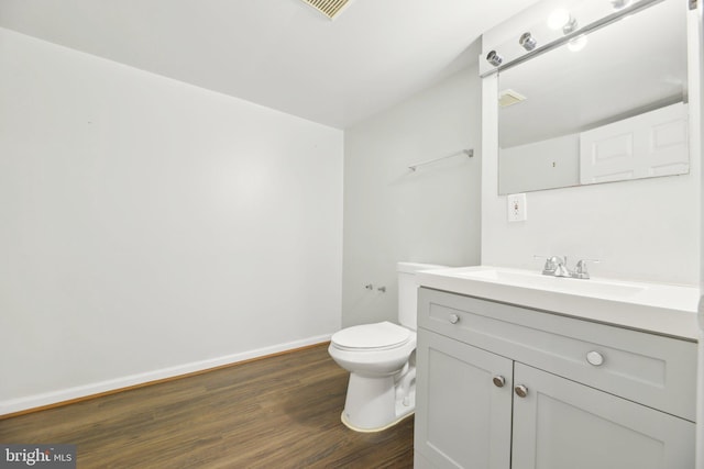half bath with baseboards, wood finished floors, vanity, and toilet
