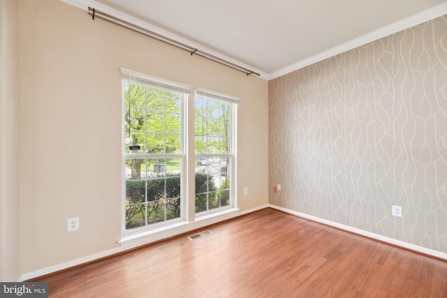 empty room with visible vents, baseboards, wood finished floors, and ornamental molding