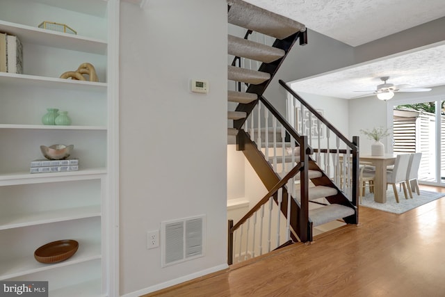 staircase featuring visible vents, a ceiling fan, a textured ceiling, and wood finished floors