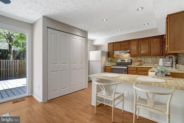 kitchen with a sink, light countertops, a peninsula, electric stove, and under cabinet range hood