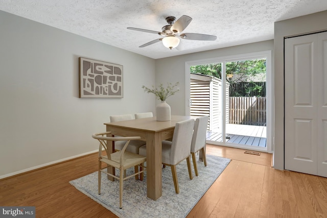 dining area with light wood-style floors, baseboards, ceiling fan, and a textured ceiling