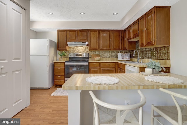 kitchen with a sink, under cabinet range hood, white appliances, and light countertops