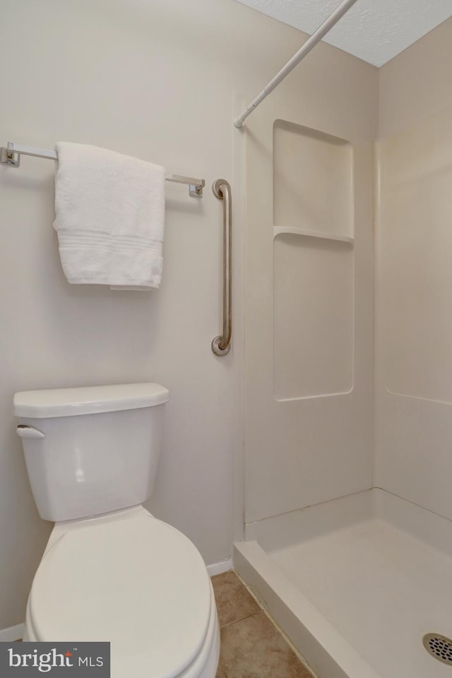 bathroom featuring toilet, baseboards, and a shower stall