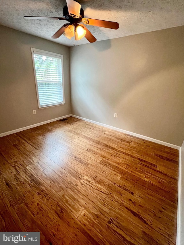 empty room with hardwood / wood-style floors, ceiling fan, baseboards, and a textured ceiling
