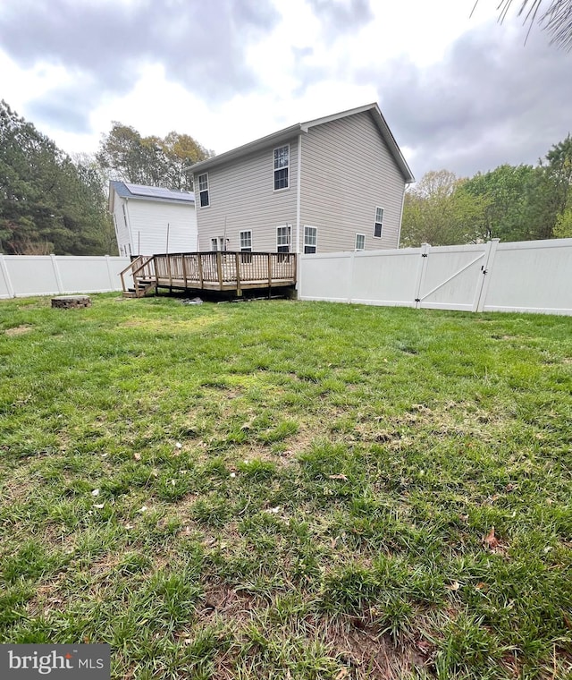 rear view of property with a fenced backyard, a wooden deck, a gate, and a lawn