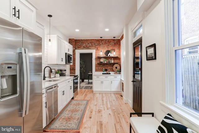 kitchen with open shelves, a sink, brick wall, white cabinets, and appliances with stainless steel finishes