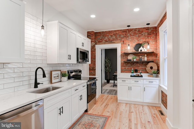 kitchen featuring stainless steel appliances, a sink, white cabinetry, and brick wall