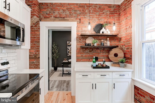 kitchen with light wood-type flooring, brick wall, appliances with stainless steel finishes, and plenty of natural light