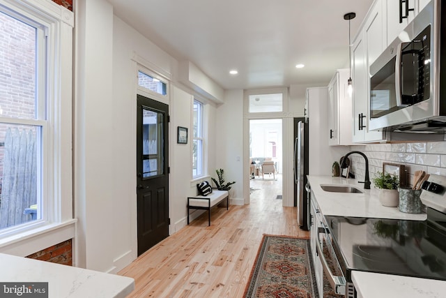 kitchen with white cabinets, stainless steel appliances, a sink, light wood-type flooring, and decorative backsplash