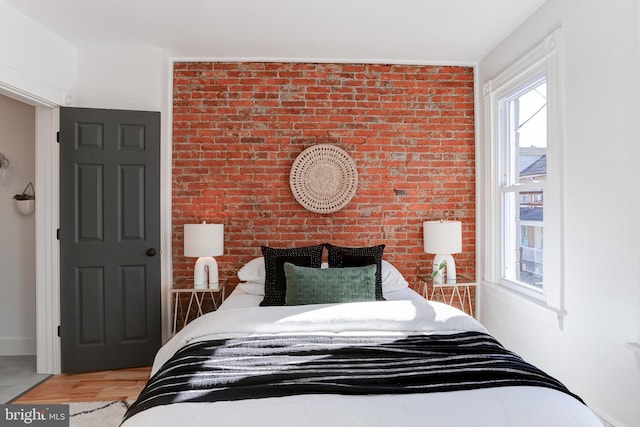 bedroom featuring brick wall and wood finished floors