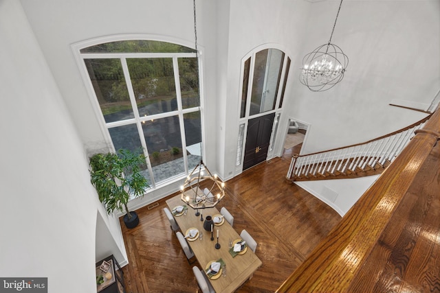 living area featuring stairway, wood finished floors, a towering ceiling, a notable chandelier, and visible vents