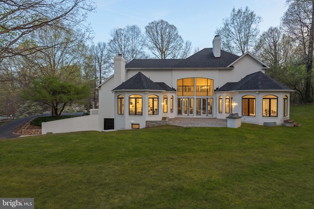 back of property with a lawn, a chimney, roof with shingles, and stucco siding