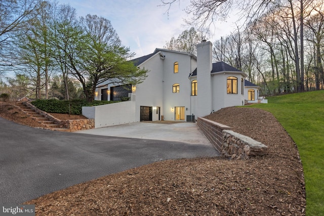 view of home's exterior with stucco siding, cooling unit, a chimney, and aphalt driveway