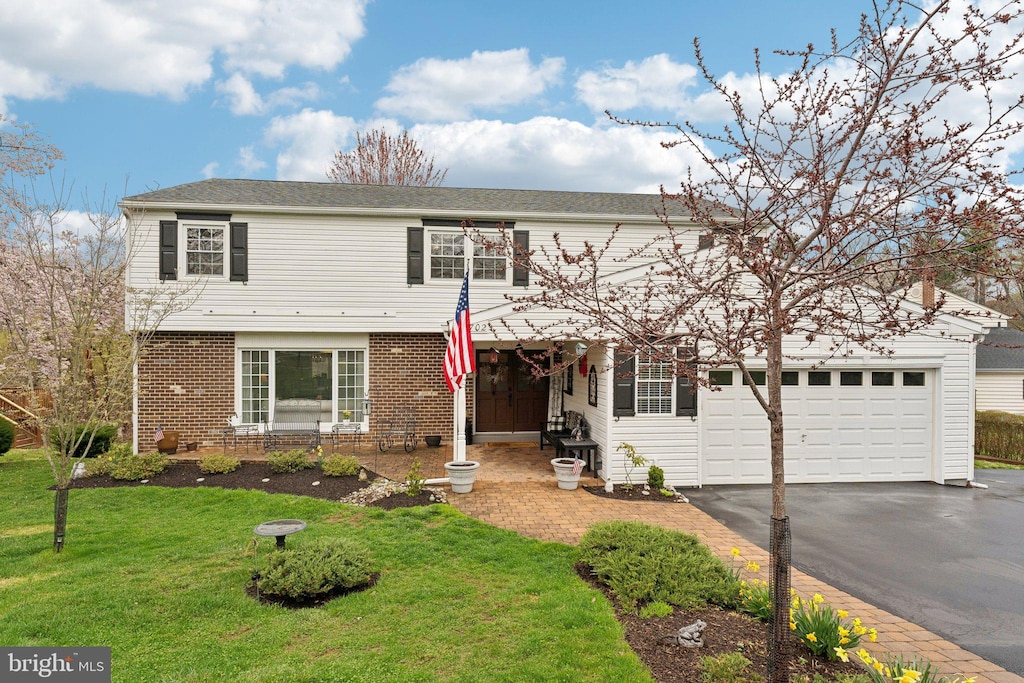view of front of home featuring an attached garage, driveway, a front yard, and brick siding