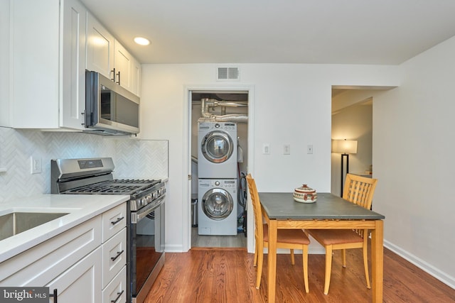 kitchen with stacked washer and dryer, white cabinetry, visible vents, appliances with stainless steel finishes, and wood finished floors