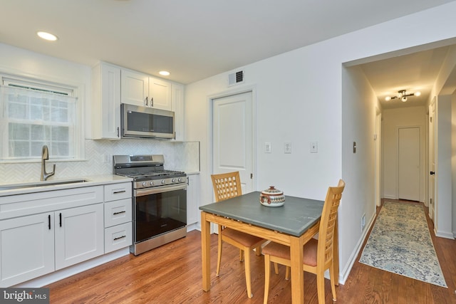kitchen featuring visible vents, a sink, light wood finished floors, stainless steel appliances, and backsplash