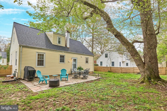 rear view of property with a yard, roof with shingles, a patio area, fence, and a chimney