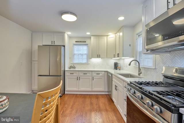 kitchen featuring light wood-style flooring, backsplash, white cabinets, stainless steel appliances, and a sink