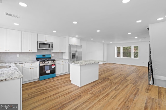 kitchen with tasteful backsplash, visible vents, a center island, stainless steel appliances, and light wood-style flooring