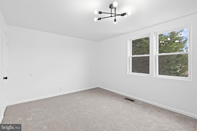 carpeted spare room featuring visible vents, baseboards, and a notable chandelier