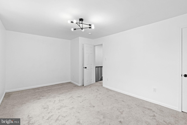 carpeted spare room featuring a notable chandelier and baseboards