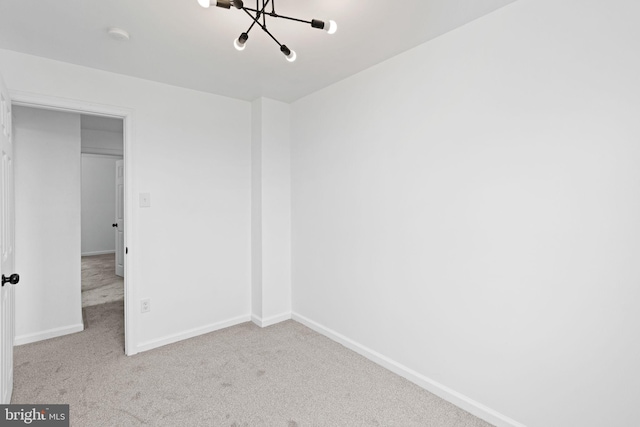 empty room featuring a chandelier, baseboards, and carpet floors