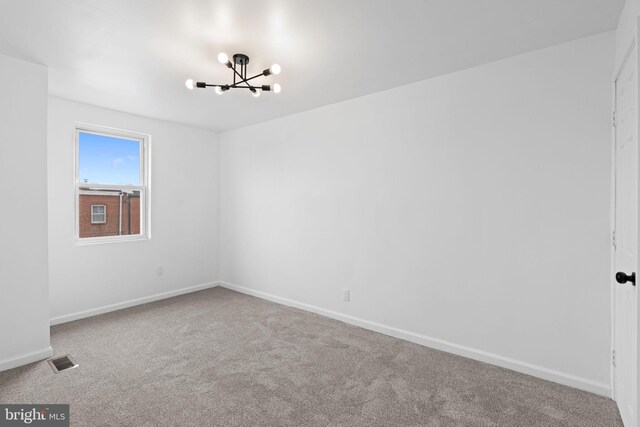 spare room with carpet flooring, visible vents, baseboards, and an inviting chandelier